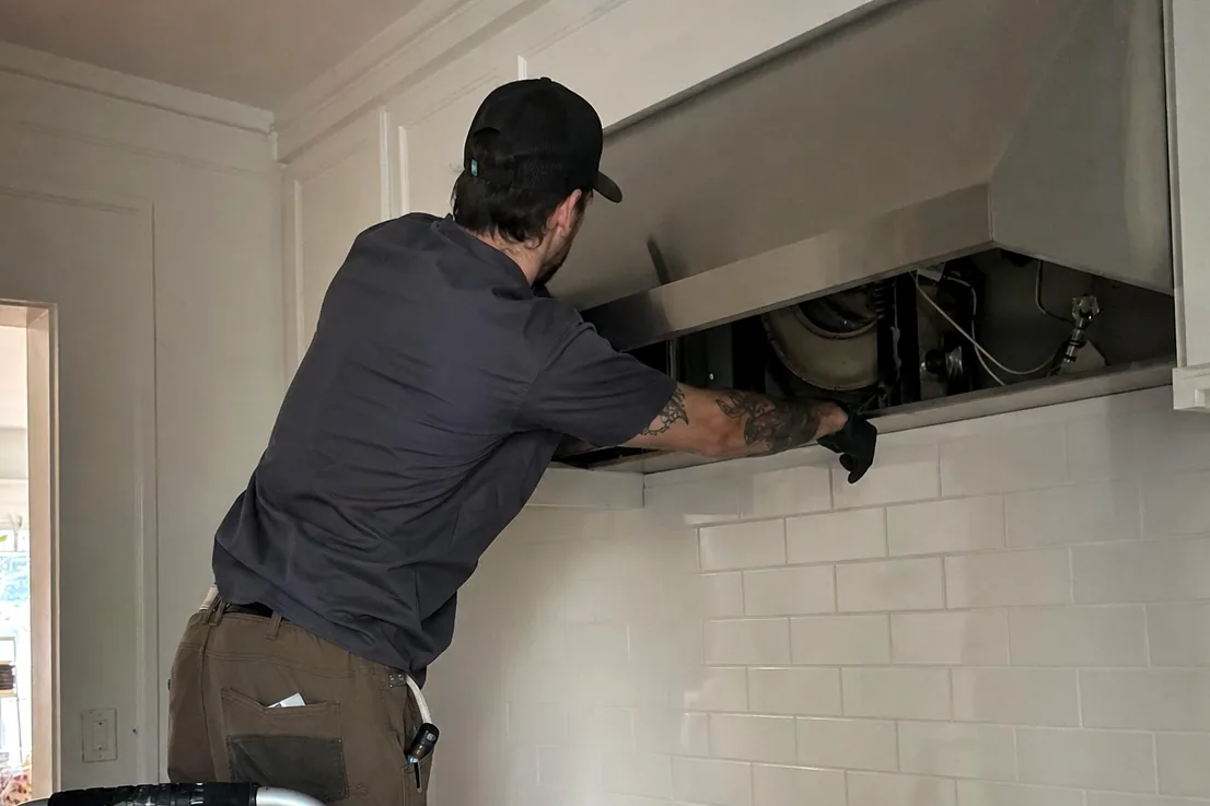 A technician working overhead in a tiled kitchen with the cooking appliance opened below him